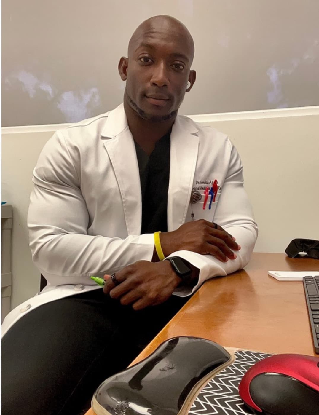Dr. Emeka Ajufo in a white coat at a desk, looking at the camera.